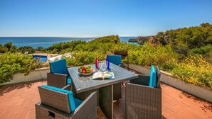 A patio with wicker furniture, a table with a book and fruit, and a view of the sea. - Quinta Jordia - Twelve Bedroom Villa, Sleeps 26 (Lagoa)