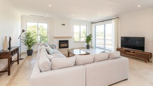 A spacious living room with a large sofa, a fireplace, a television, and large windows. - Villa Catao - Four Bedroom Villa, Sleeps 8 (Almansil)