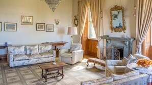 A classic living room with a floral sofa, a wooden coffee table, a fireplace, and a chandelier. - Villa Quinta Santa Luzia (Funchal)