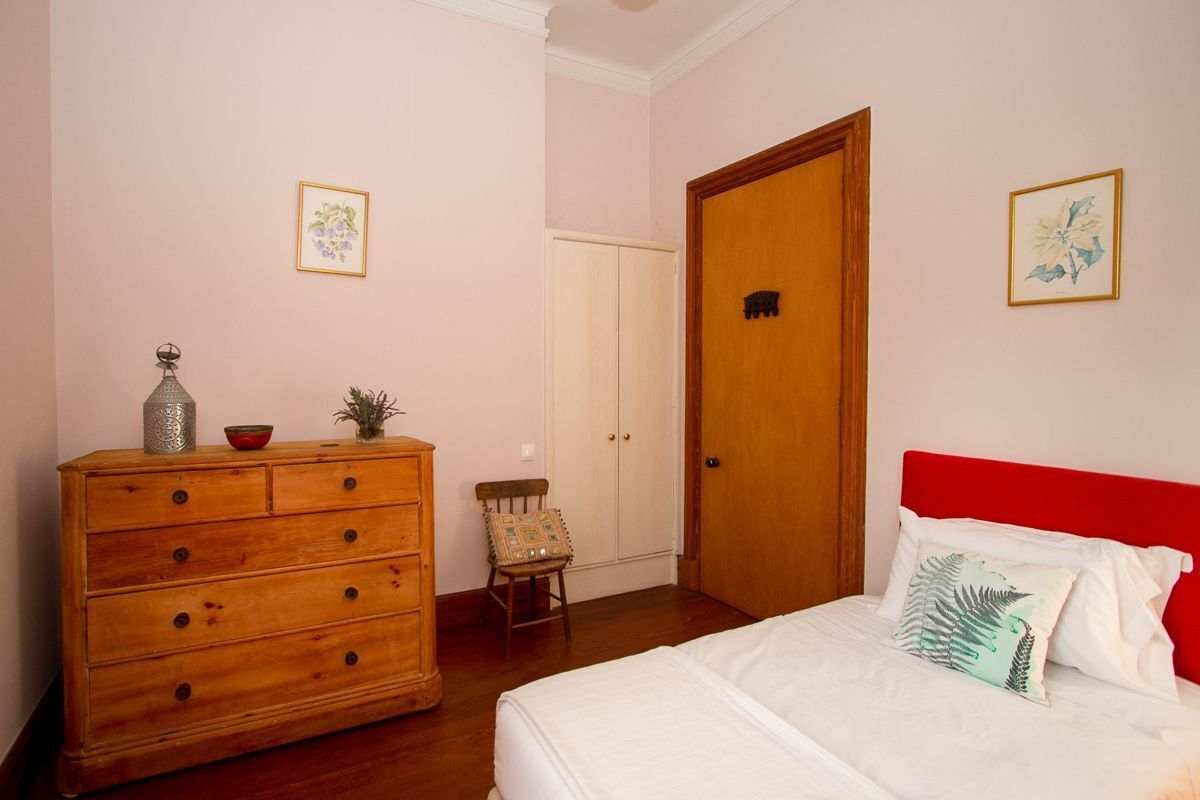 A bedroom with a wooden dresser, a chair, a bed with white bedding, and a red headboard.