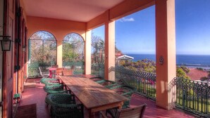 A covered outdoor seating area with a wooden table and wicker chairs, overlooking a scenic view of the ocean and surrounding landscape. - Villa Quinta Santa Luzia (Funchal)