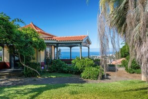 A traditional building with a tiled roof, surrounded by lush greenery and a view of the sea. - Villa Quinta Santa Luzia (Funchal)
