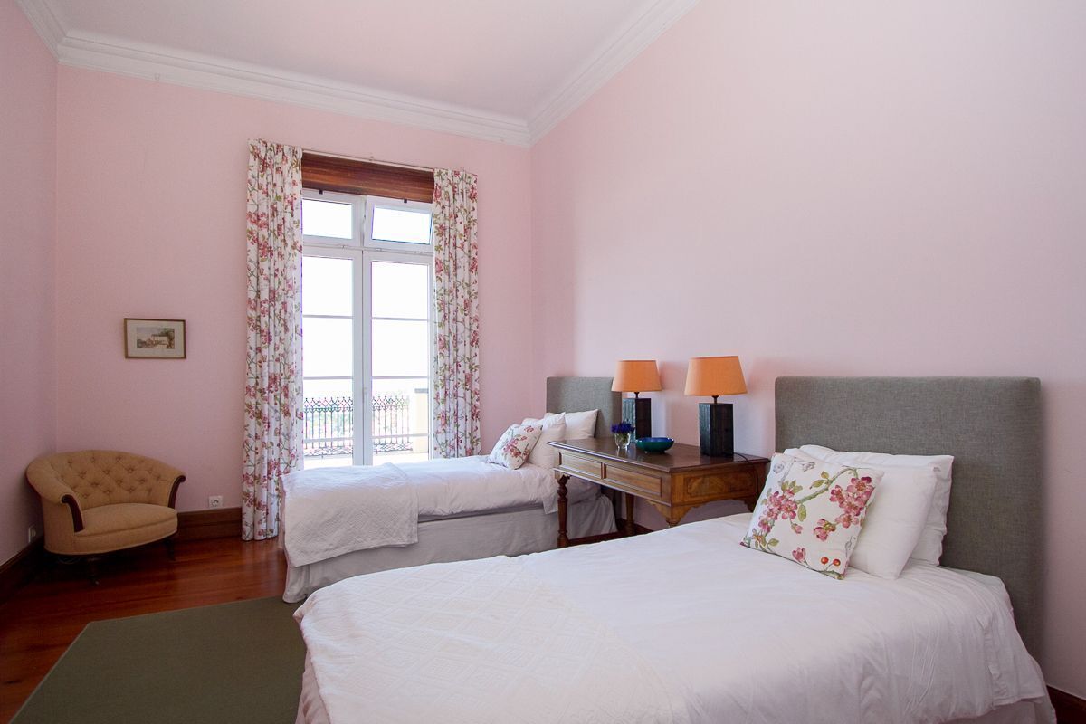 Une chambre d’hôtel avec deux lits simples, un bureau avec des lampes, une chaise et une fenêtre avec des rideaux à motifs floraux.