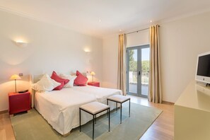 A hotel room with a large bed, two bedside tables, a TV, and a balcony with curtains.