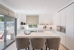 Uma cozinha moderna com uma ilha grande, três cadeiras e vista para o exterior.