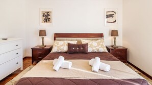 Une chambre d’hôtel bien aménagée, avec un grand lit, deux tables de chevet avec des lampes, une commode et des œuvres d’art accrochées aux murs.