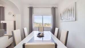 A modern dining room with a glass table, six chairs, and a view of the outdoors through large windows. - Villa Botela - Three Bedroom Villa, Sleeps 6 (Lagoa)