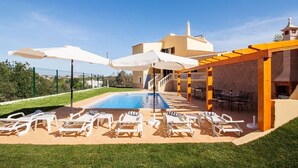 A swimming pool with lounge chairs and umbrellas, surrounded by a well-maintained lawn and a building with a tiled roof. - Villa Botela - Three Bedroom Villa, Sleeps 6 (Lagoa)