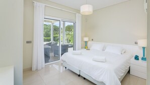 A modern bedroom with a large bed, a sliding glass door to a balcony, and two bedside lamps.