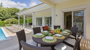 An outdoor dining area with a pool, lounge chairs, and a covered patio.
