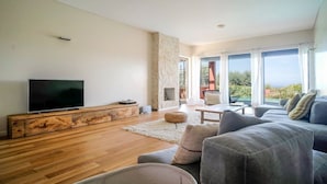 Una sala de estar moderna con un televisor de pantalla plana, piso de madera, una chimenea de piedra y un balcón con vistas.