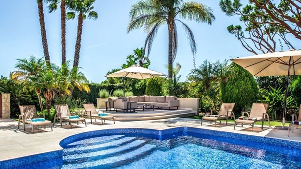A swimming pool with lounge chairs and umbrellas, surrounded by palm trees and greenery. - Villa Lella - Five Bedroom Villa, Sleeps 10 (Almansil)