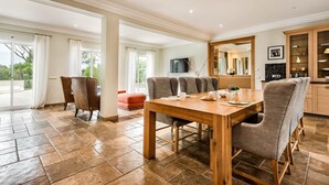 A spacious dining area with a wooden table and six chairs, large windows with curtains, and a view of greenery outside. - Villa Lella - Five Bedroom Villa, Sleeps 10 (Almansil)