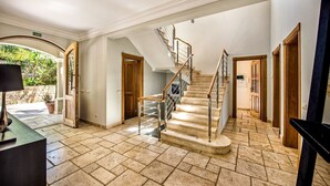 A spacious interior with a stone-tiled floor, a central staircase, and a view of greenery outside. - Villa Lella - Five Bedroom Villa, Sleeps 10 (Almansil)