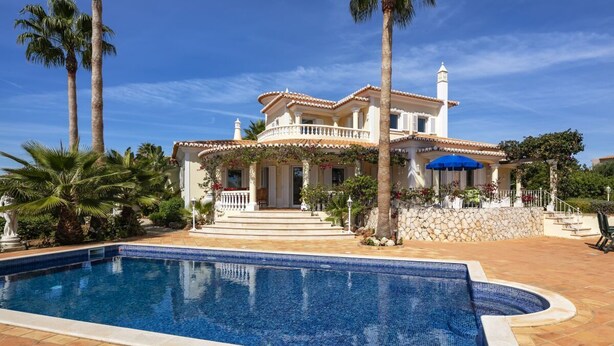 Una amplia casa con piscina, rodeada de palmeras y un cielo azul despejado.
