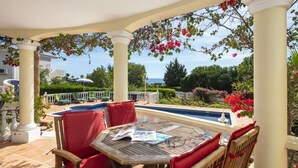 Un espacio de estar al aire libre cubierto con piscina, sillas rojas y una mesa con revistas y vasos.