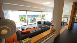 A modern living room with a large window, a sofa, a coffee table, and a bookshelf. - Villa Esqueiro - Three Bedroom Villa, Sleeps 6 (Moledo)