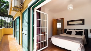 Une chambre à coucher comprenant un lit, une table de chevet, une fenêtre et une porte donnant sur un espace extérieur.