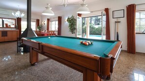 Une table de billard dans une pièce dotée d’une grande fenêtre, d’un miroir et d’un lustre.