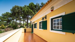 Un bâtiment jaune avec des volets verts et une terrasse carrelée.