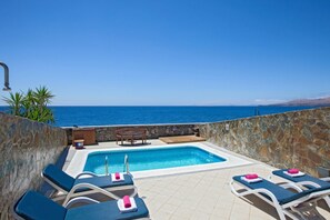 Un espace piscine doté de chaises longues et d’un jacuzzi, avec vue sur la mer.