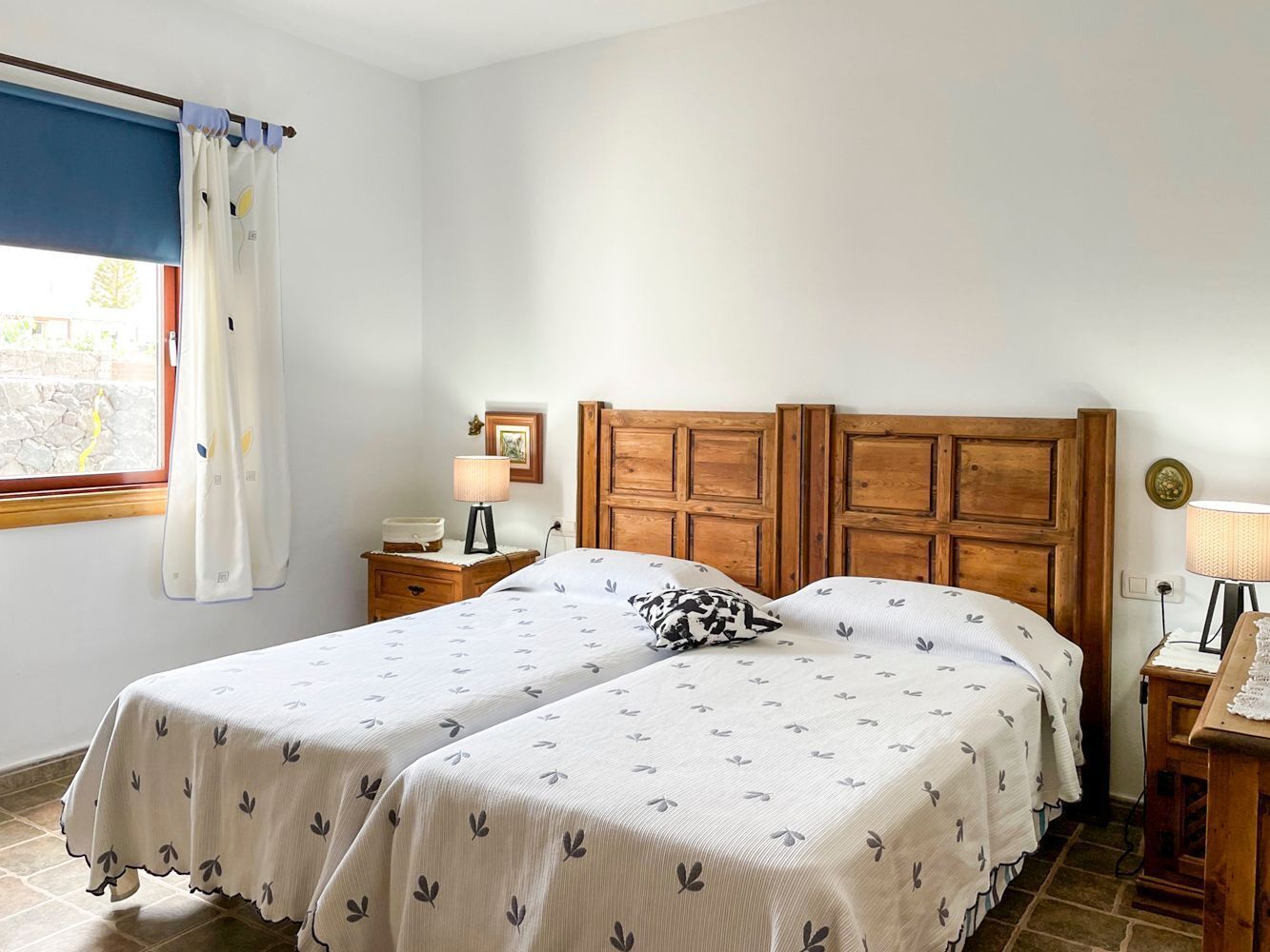 Un letto matrimoniale con testiera in legno, due comodini con lampade e una finestra con tende.
