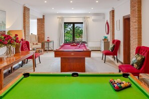 A pool table with balls, a red sofa, a wooden coffee table, and a chair with a cushion.