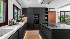 Une cuisine moderne dotée d’un îlot central, d’appareils électroménagers intégrés et offrant une vue sur l’extérieur.