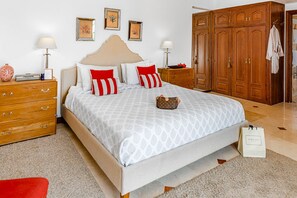 A bedroom with a bed, wooden wardrobe, bedside tables, and a red chair.