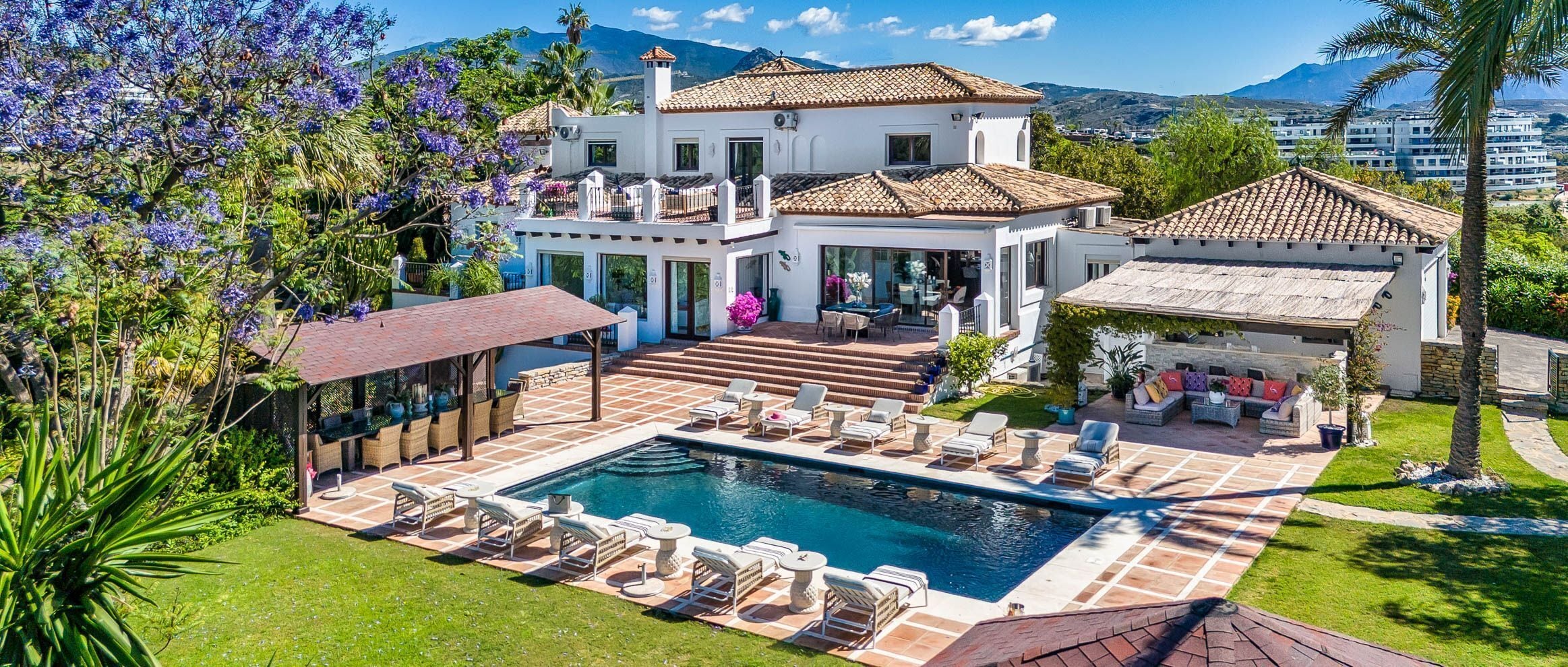 A two-story house with a swimming pool, outdoor seating, and a garden.