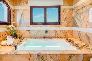 A bathroom with a marble wall, a bathtub, a window, and a towel rack.