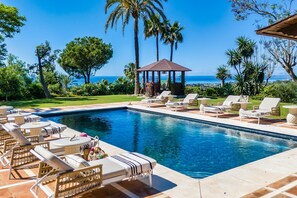 A pool area with lounge chairs and a gazebo overlooking a body of water.