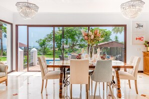 A dining area with a large table, chairs, and a view of a pool and greenery. - Villa Lola - Five Bedroom Villa, Sleeps 10 (Estepona)