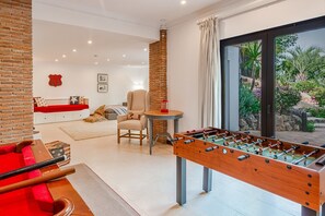 Een moderne woonkamer met een tafelvoetbalspel, een rode bank en een wand van baksteen.