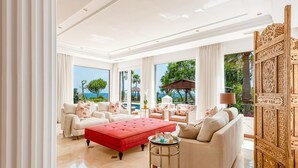 Un salon spacieux avec un grand pouf rouge, de nombreux sièges et une vue sur l’océan.