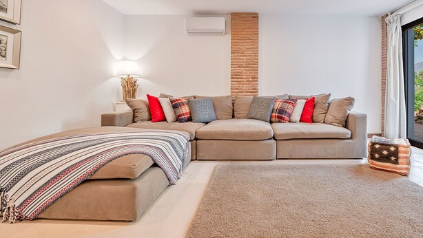 Een moderne woonkamer met een hoekbank, een geborduurde plaid en een bijzettafeltje.