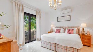 Een slaapkamer met een groot bed, een bureau, een stoel, een kroonluchter en uitzicht op de omgeving.