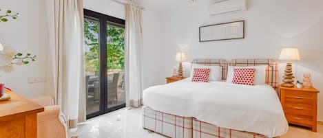 A bedroom with a large bed, a desk, a chair, a chandelier, and a view of the outdoors.