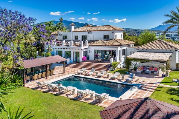 A two-story house with a swimming pool, outdoor seating, and a view of the mountains.