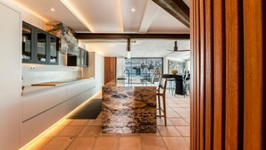 A modern kitchen with a marble island, built-in appliances, and a dining area with a view. - Villa Adaline - Five Bedroom Villa, Sleeps 10 (Alcaucín)