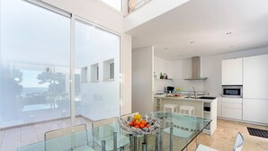 Une cuisine moderne avec des meubles blancs, une table à manger en verre et un saladier rempli de fruits.