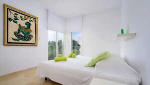 Une chambre moderne avec un lit, une petite table, un coussin vert, une serviette verte et une œuvre d’art encadrée accrochée au mur.