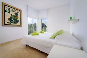 Un dormitorio moderno con cama, una mesita, un cojín verde y una toalla verde, además de una obra de arte enmarcada en la pared.