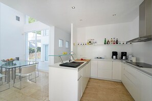 A modern kitchen with a glass dining table, white cabinetry, and a variety of kitchen appliances.