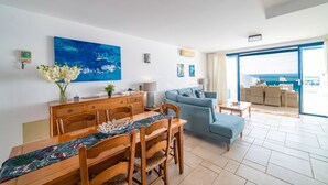 Un vaste espace de vie comprenant une table à manger, un canapé et une grande fenêtre donnant sur la mer.