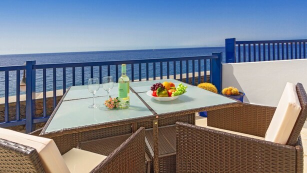 Un balcon agrémenté de meubles en osier, d’une table en verre et d’un panier de fruits.