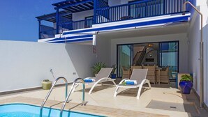 Un espace piscine extérieur moderne, doté d’une piscine à l’eau d’un bleu limpide, de chaises longues blanches et d’un balcon avec des rampes bleues.