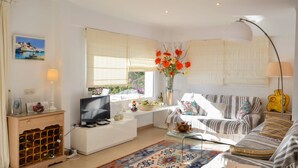A living room with a TV, sofa, and a window with curtains. - Villa Petunies - Three Bedroom Villa, Sleeps 6 (Begur)
