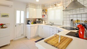 A modern kitchen with white cabinets, a microwave, a kettle, and a cutting board with a knife. - Villa Petunies - Three Bedroom Villa, Sleeps 6 (Begur)