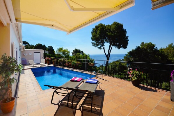 Ein Poolbereich mit Blick auf das Meer, einem Tisch mit Stühlen und Topfpflanzen.